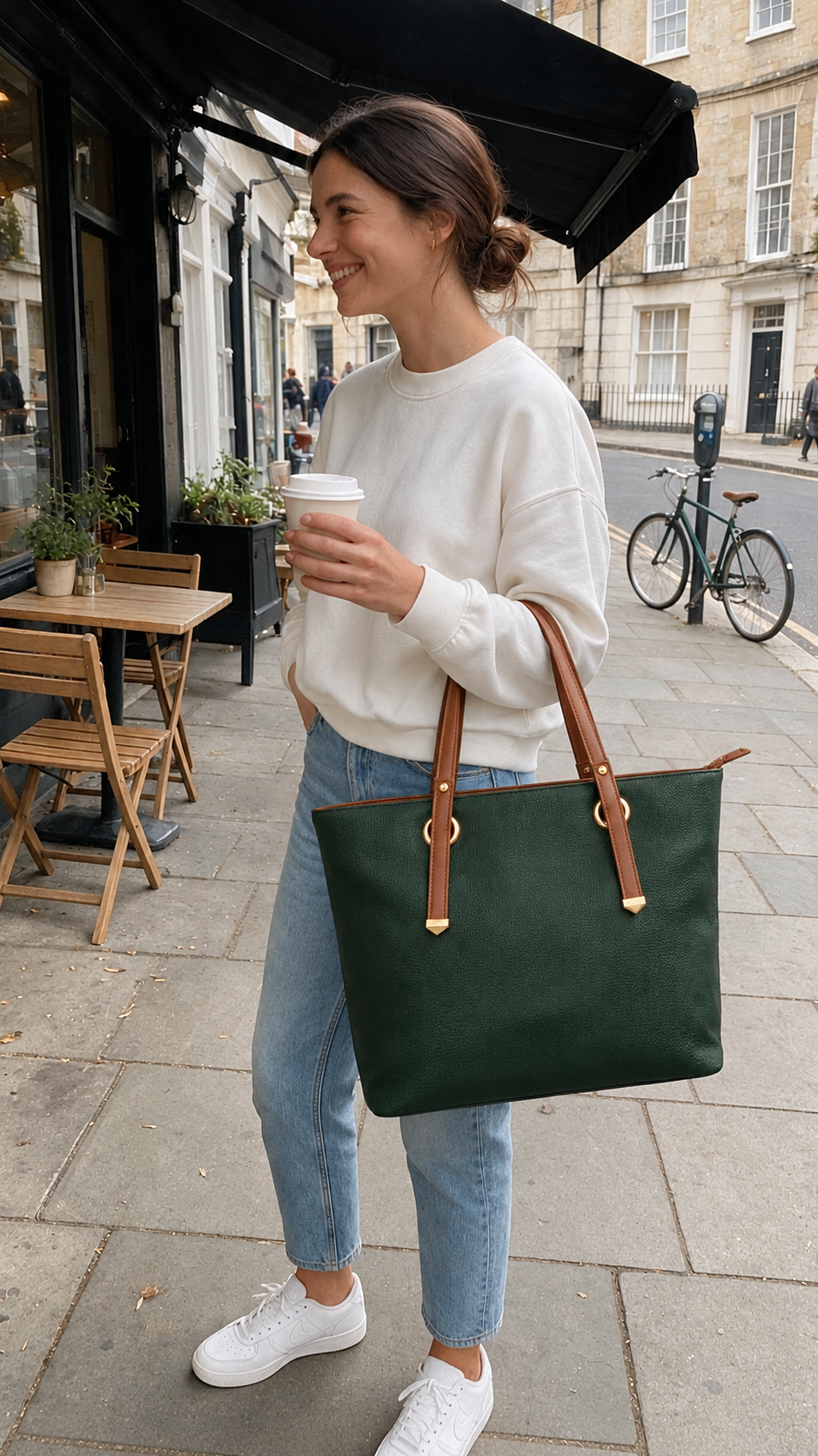 Modern Hola Shoulder Bag in forest green with brown shoulder handles, carried by a woman in a casual cafe street-style setting