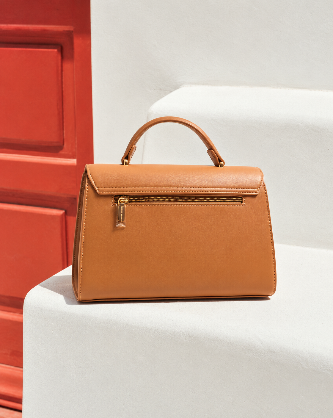 Bela Sling back view in caramel brown featuring rear zipper pocket, structured silhouette and gold-tone hardware