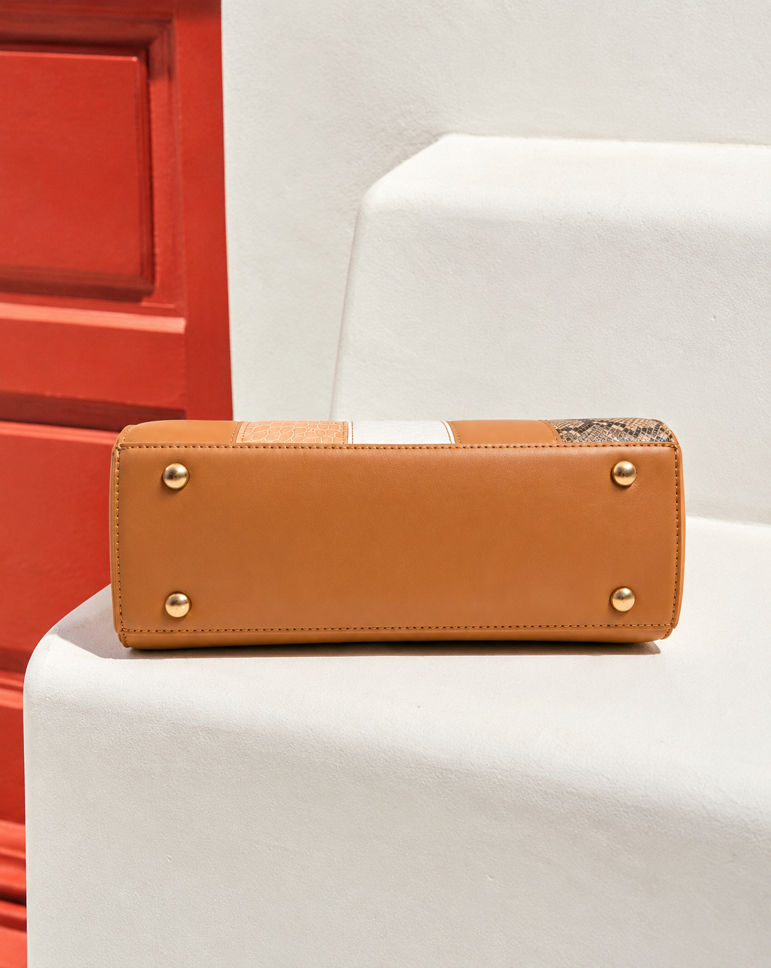 Bela Sling bottom view in caramel brown showing structured base, neat stitching and four gold-tone protective metal feet